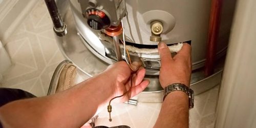 A man uses a flashlight to help him see the hot water heater in a dark closet A man uses a flashlight to help him see the hot water heater in a dark closet